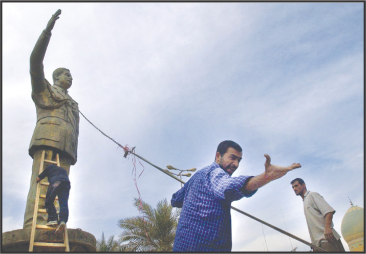 Photo: men prepare to pull down a statue of Saddam Hussein with ropes.