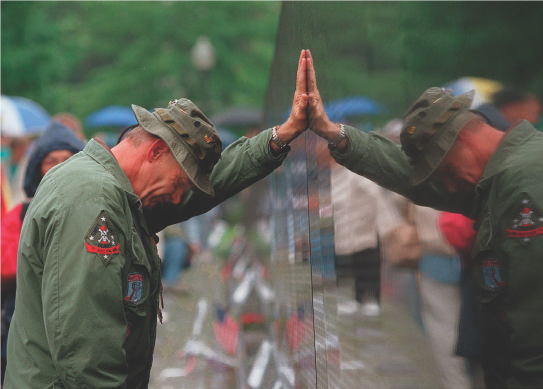 Photo: a man in military fatigues rests his hand on the Vietnam Memorial wall and cries. 