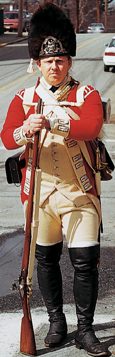 A British soldier wears a red coat and a dark fur hat.