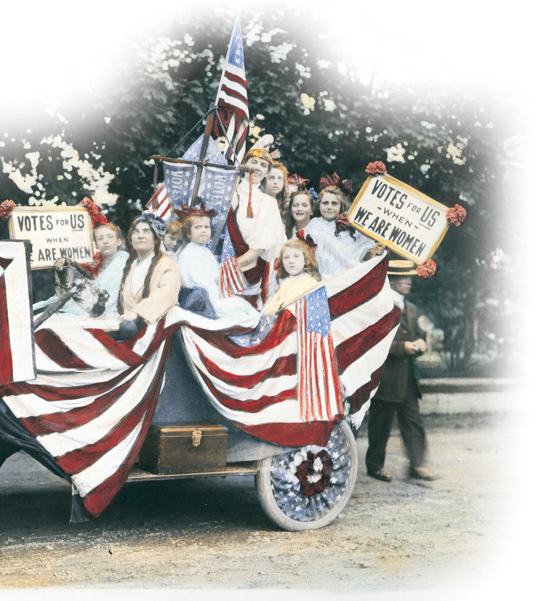 Women holding signs reading 'Votes for US When We are Women' ride in a car decorated with American flags and red, white and blue bunting.