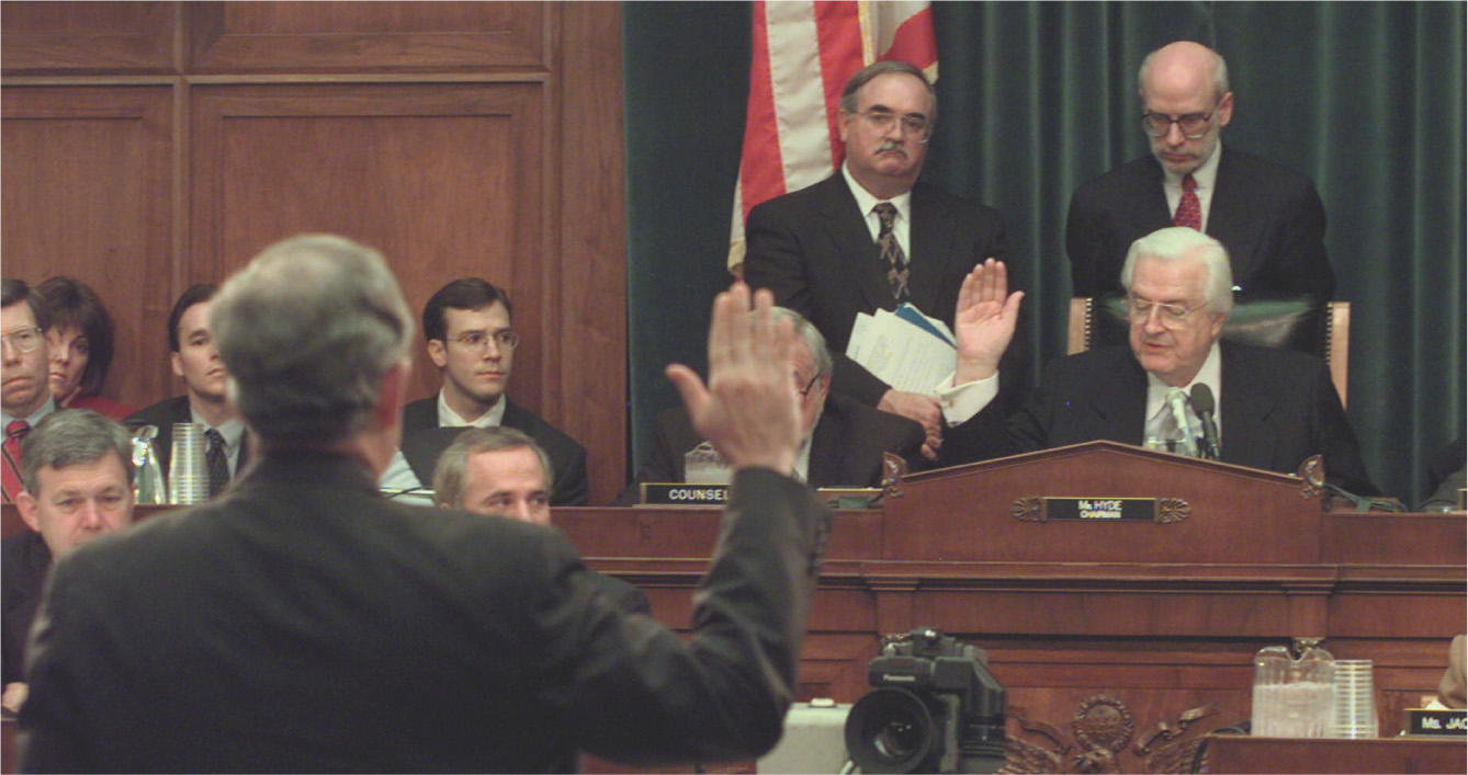 In a photo, a man stands before
a Congressional committee chairman with his hand raised.