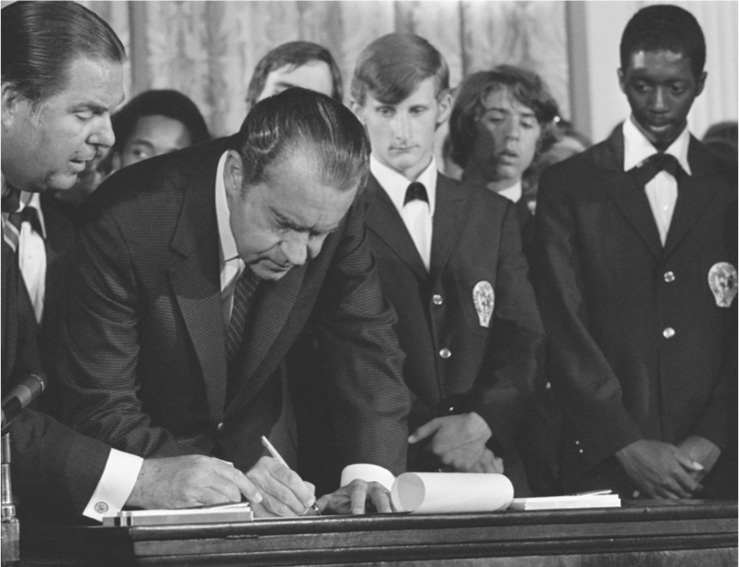 A photo: young people watch as
Richard Nixon signs a document.