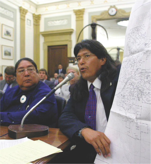 A Native American man speaks into a microphone while
holding a map.