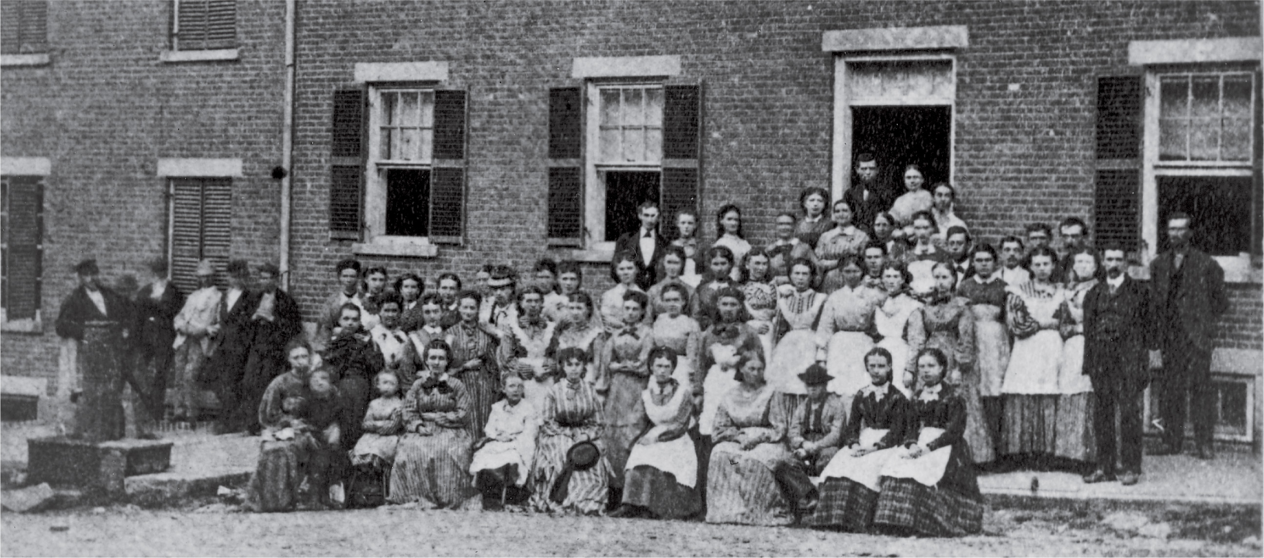 A photo shows dozens of
people posing in front of a brick boarding house.