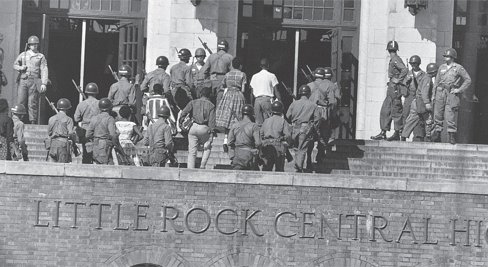 A photo: soldiers with bayonetted rifles escort African American students into Little Rock Central High School.