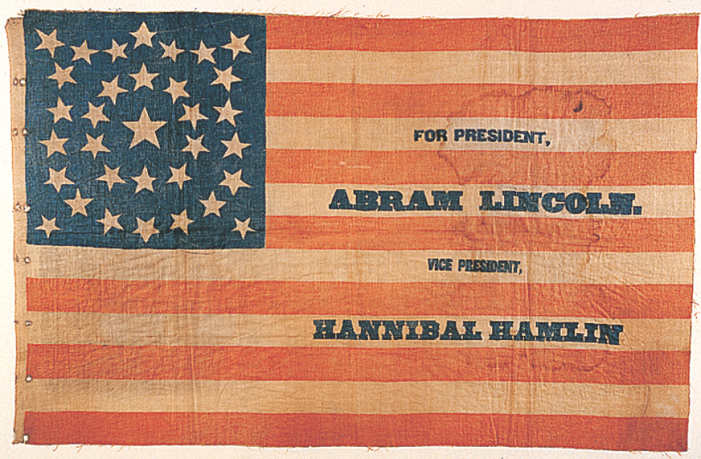 A campaign flag has stars and stripes like the American flag. It reads For President, Abram Lincoln. Vice President, Hannibal Hamlin.