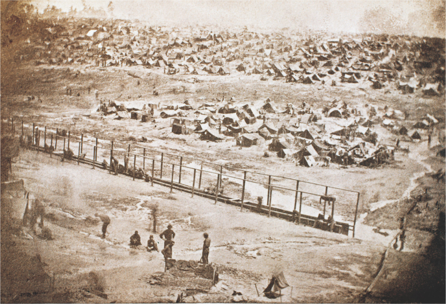 An aerial photo shows rows of tents in a field behind a fence.