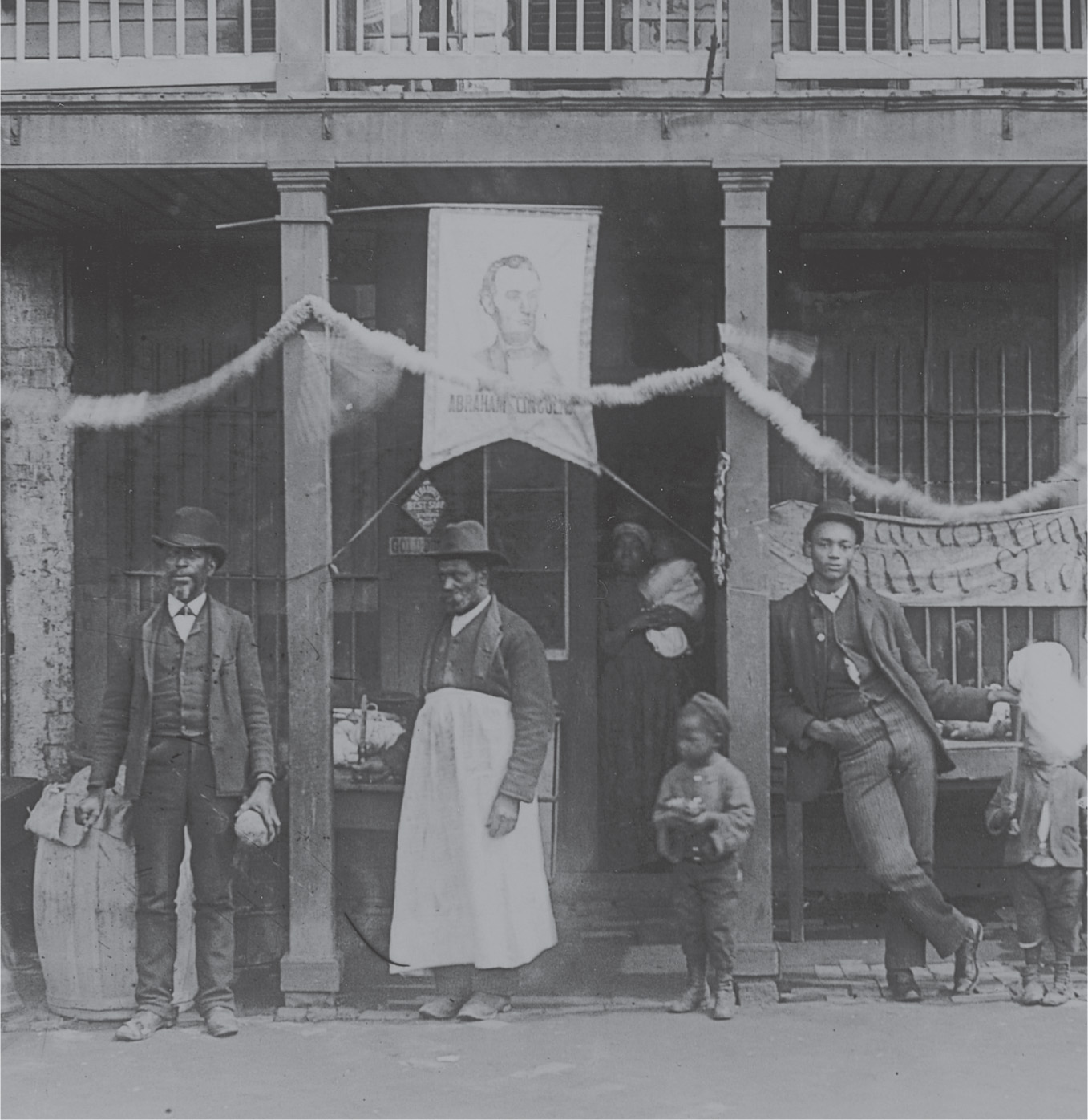A photo: African-Americans stand outside a store decorated with bunting and a picture of Abraham Lincoln.