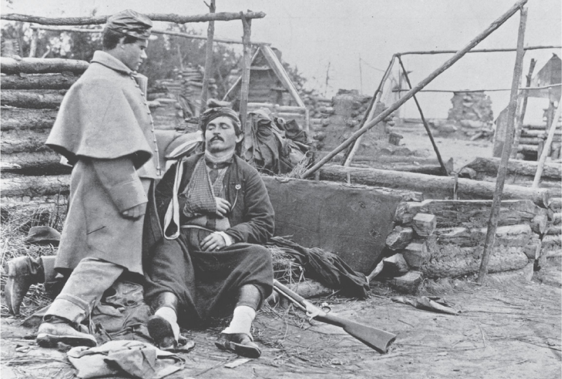 In a photo, a kneeling soldier offers his canteen to a wounded comrade.