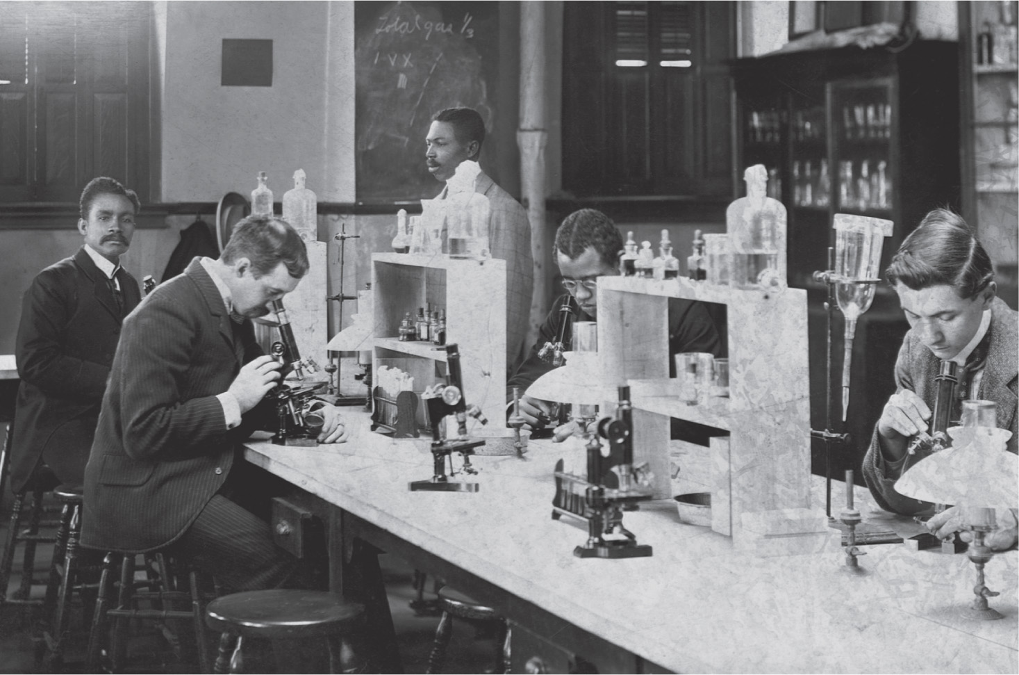 A black-and-white photo: White and African-American students work together in a lab, peering into microscopes.