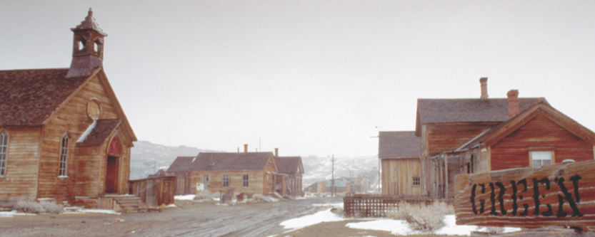Empty wood buildings line a dirt road in a deserted town.
