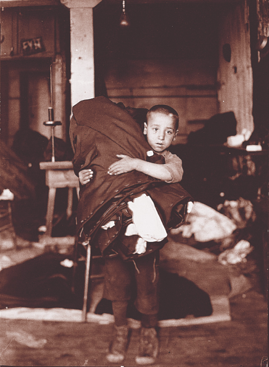 A photo: a young boy holds a big roll of canvas over his shoulder.
