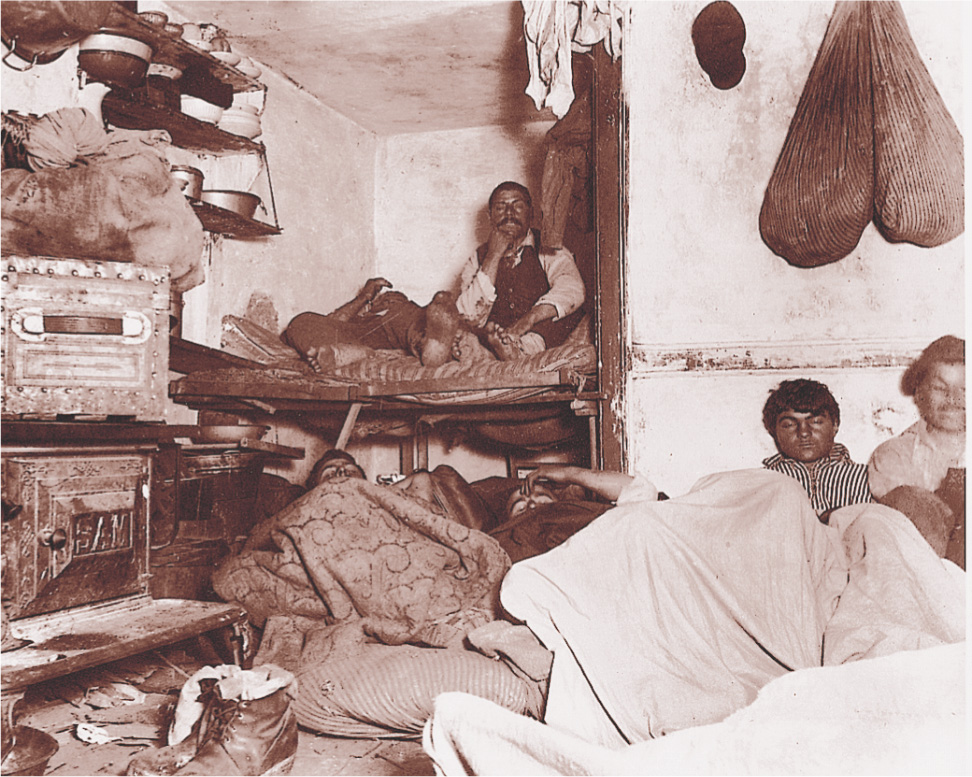 A photo: a half-dozen men sleep on the floor and in a bed in a tiny room.