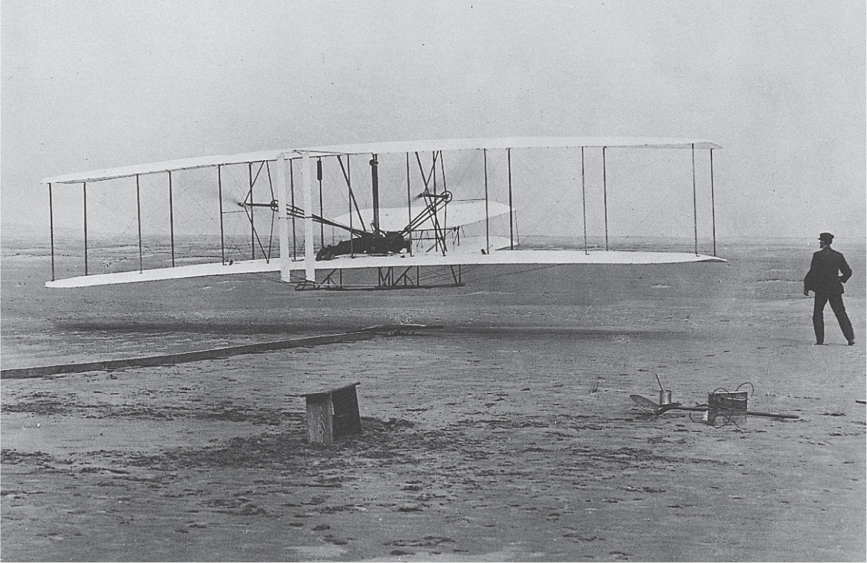 A photo: the Wright brothers' plane flies over a beach.