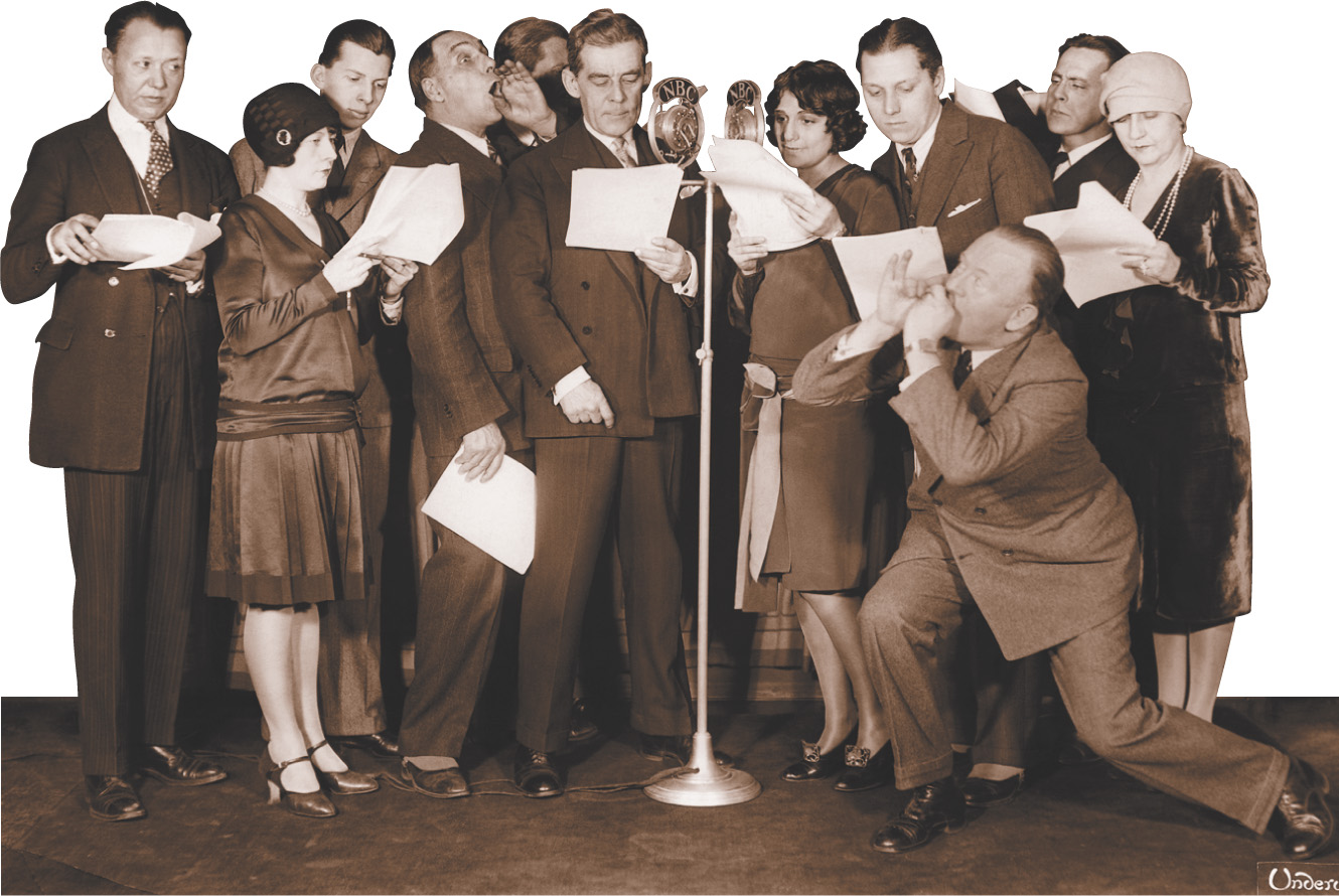 Photo: a dozen actors holding scripts cluster around a microphone