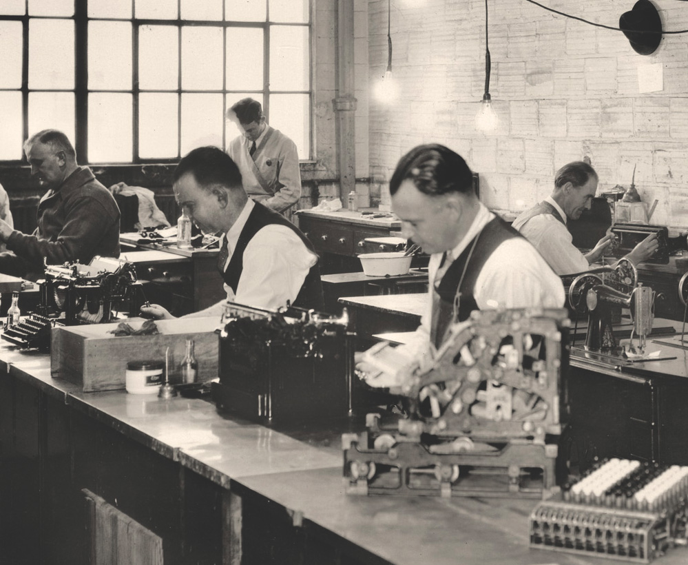 Photo: Men at workbenches with typewriters