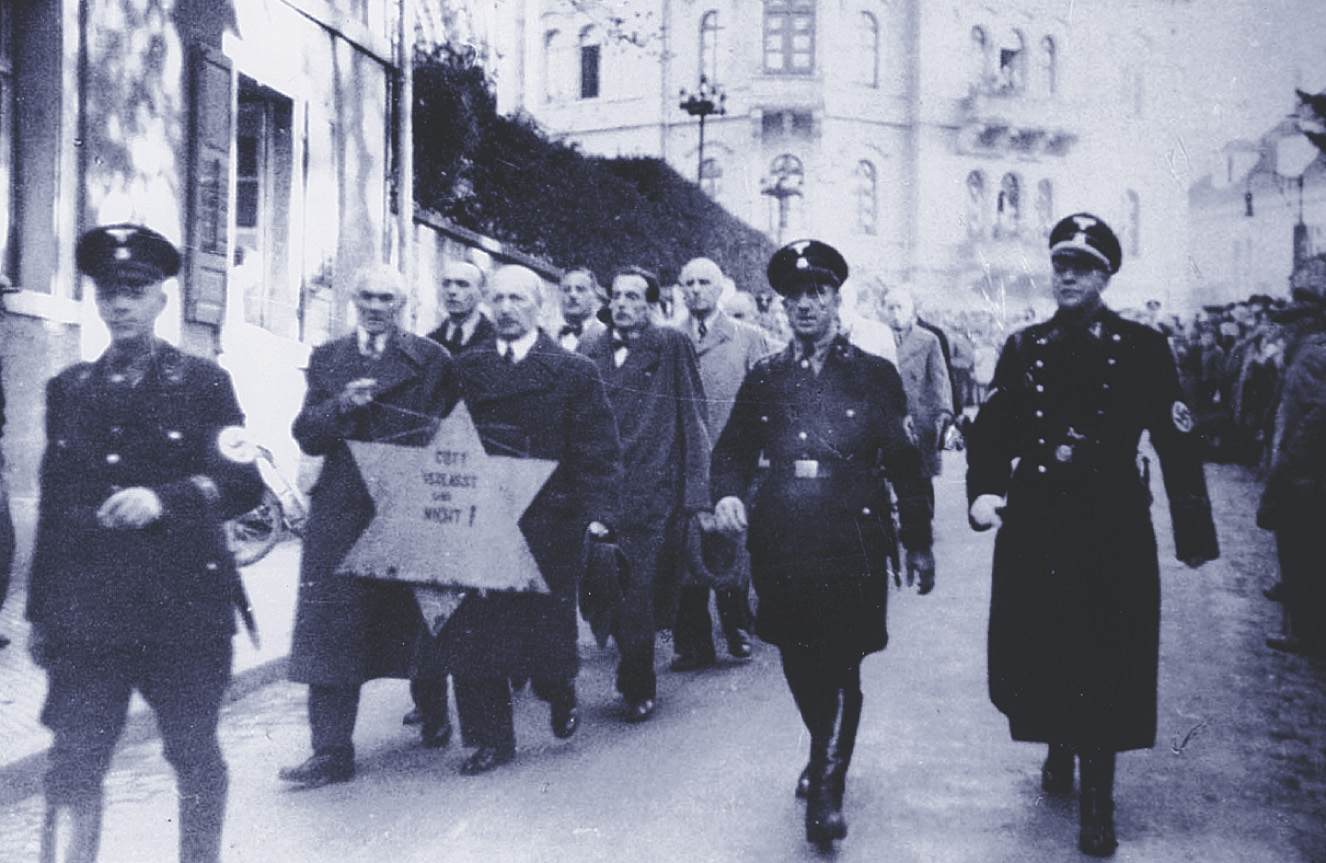 Photo: German soldiers march a column of Jewish men along a street. Men in front hold a two-foot-high Star of David.