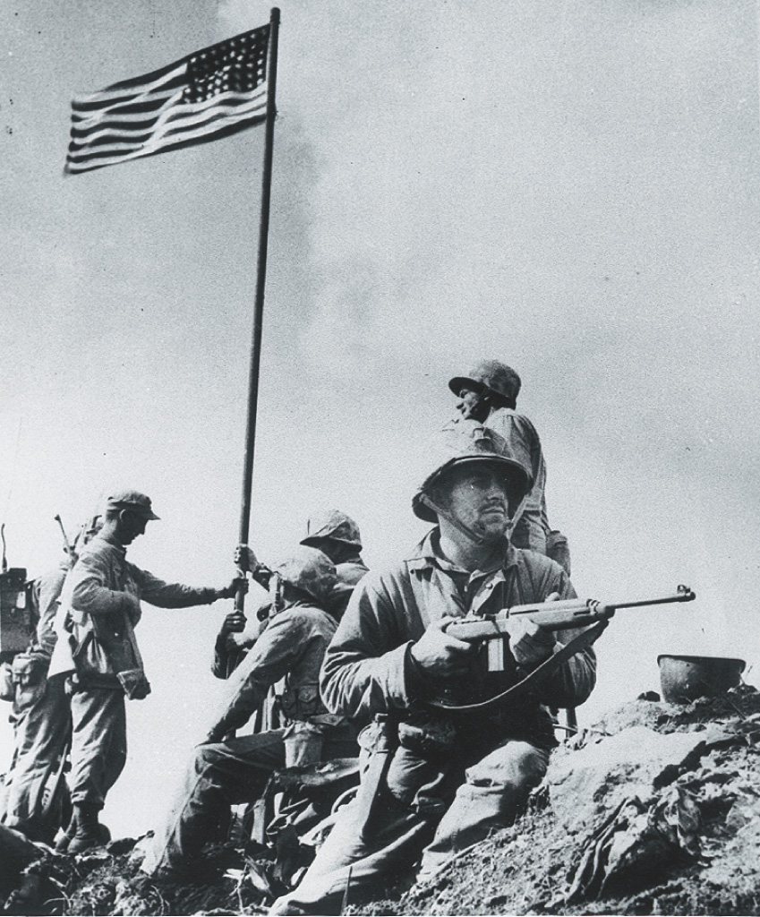 Photo: Marines lift an American flag fluttering atop a pole.