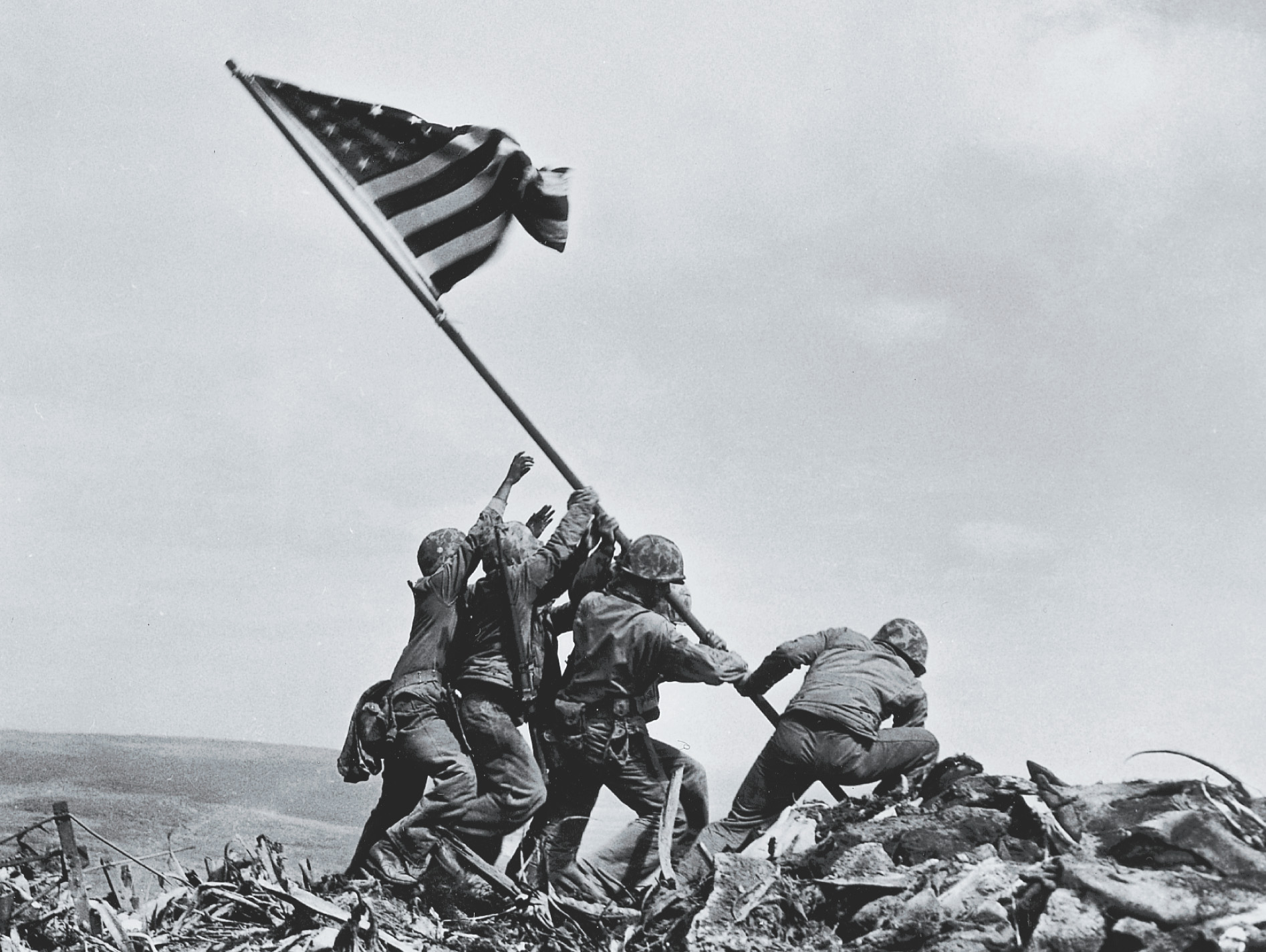 Photo: Holding a flagpole at an angle, Marines plant its end in a pile of rubble.