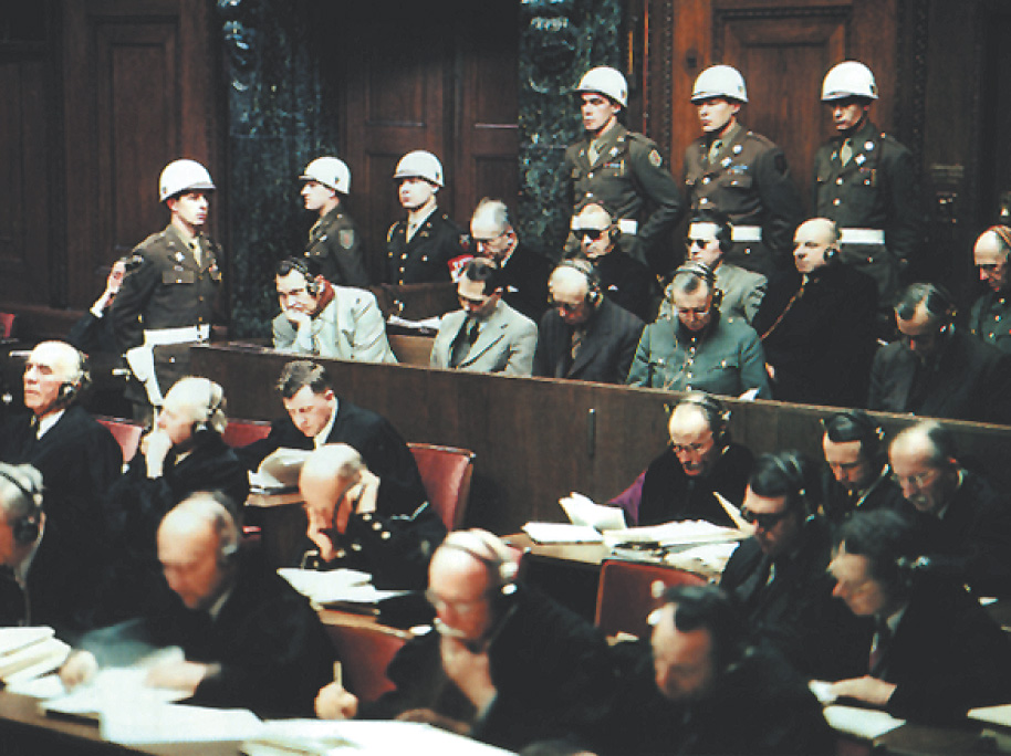 Photo: In a Nuremberg courtroom, soldiers stand at attention as men sitting in rows wear headphones