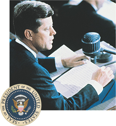 The U.S. presidential seal adorns a photo of Kennedy reading into a microphone.