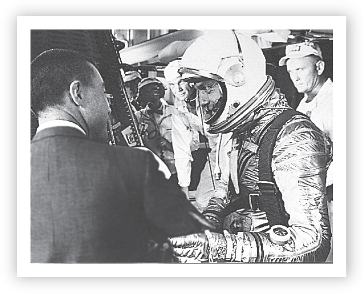 Photo: an astronaut in a spacesuit shakes hands with a man in a suit.