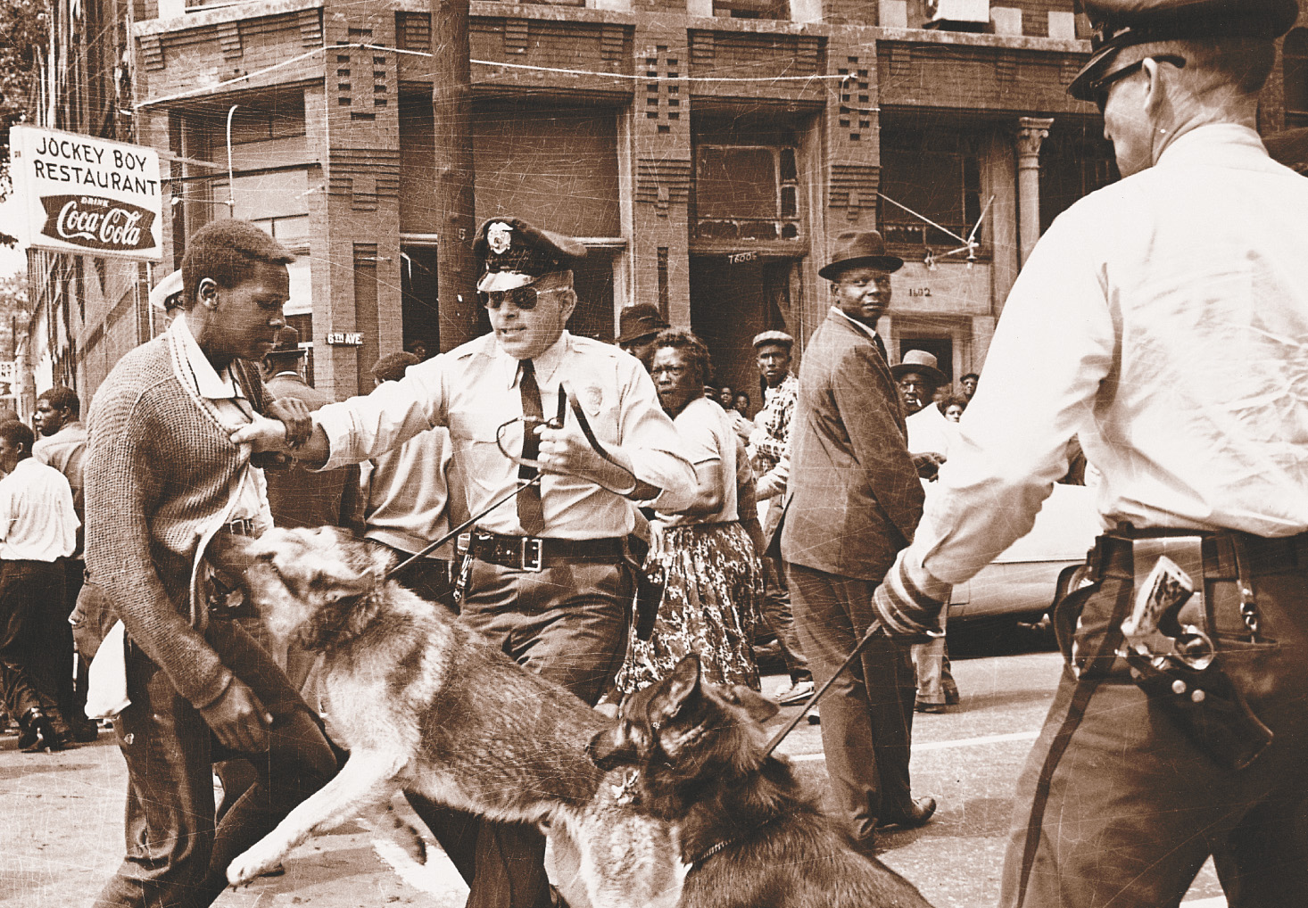 photo: a white policeman holds the leash of a dog that lunges at an African-American man.