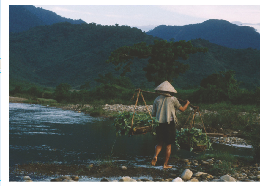 photo: a Vietnamese civillian carries bundles to a river.