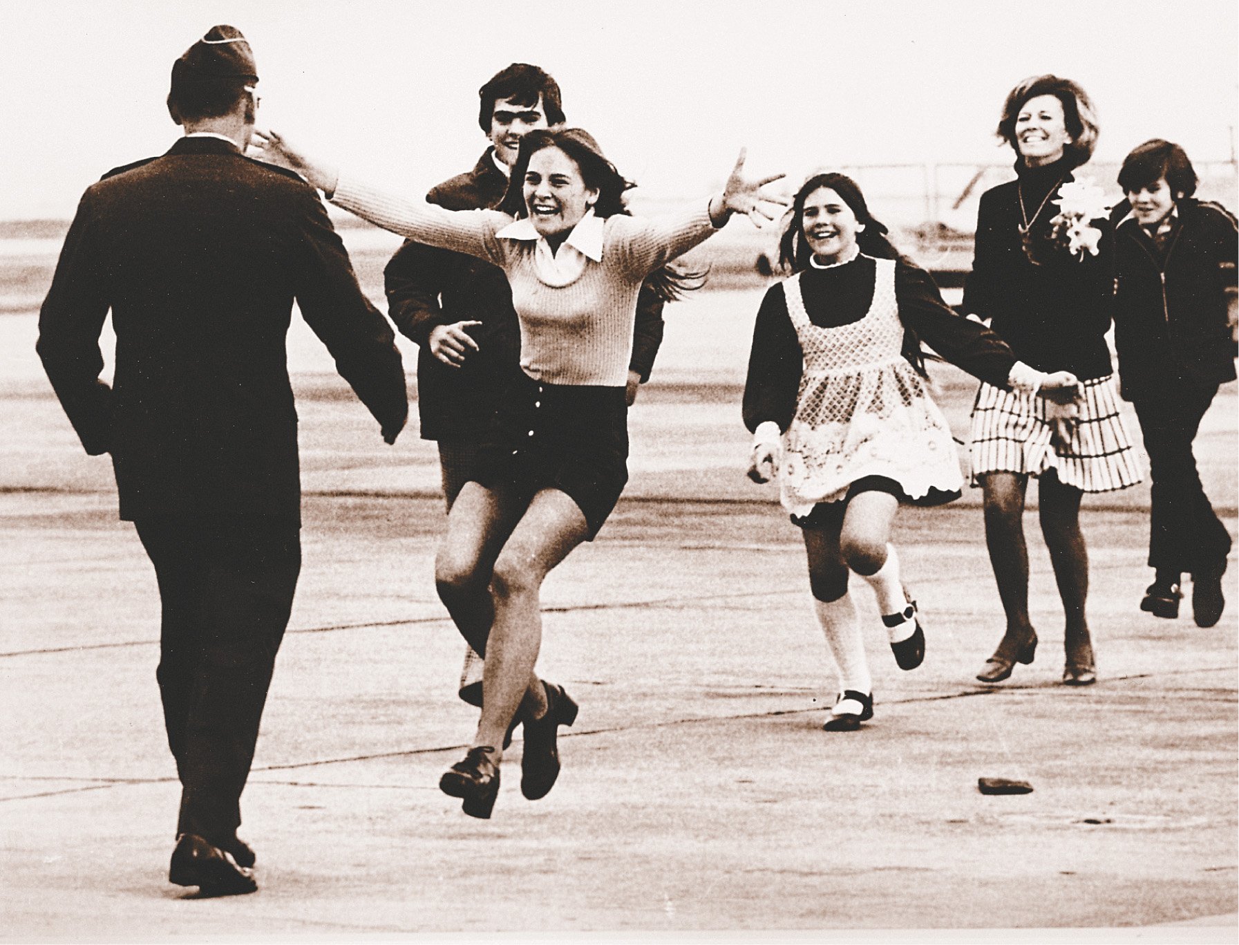 photo: on an airport runway, a man's family comes running to him.