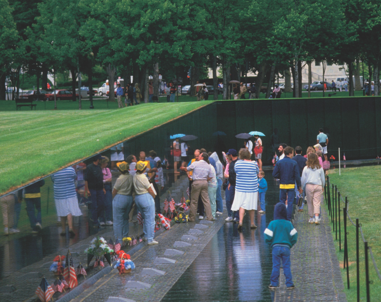 photo: visitors gather at the Vietnam Veterans Memorial. Flowers and flags line the ground by the wall.