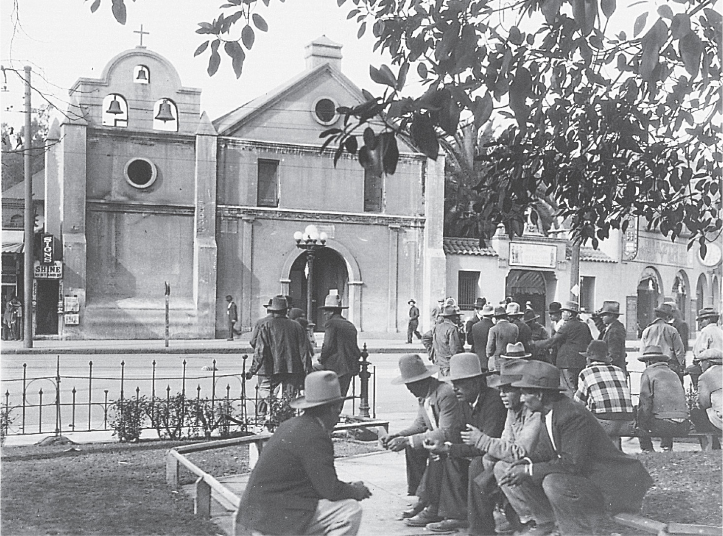 photo: men wearing broad-brimmed hats gather in a park across from a church.