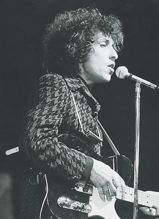 photo: Bob Dylan sings and plays an electric guitar.