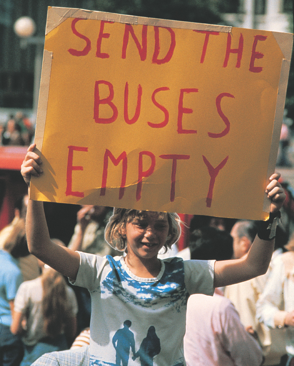 photo: a girl holds a sign that reads Send the Buses Empty.
