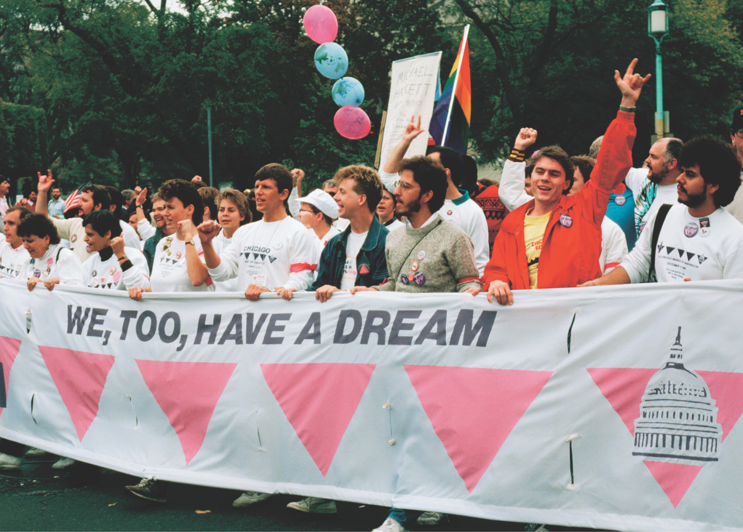 photo: people hold a banner reading 'We Too Have a Dream' adorned with pink triangles.