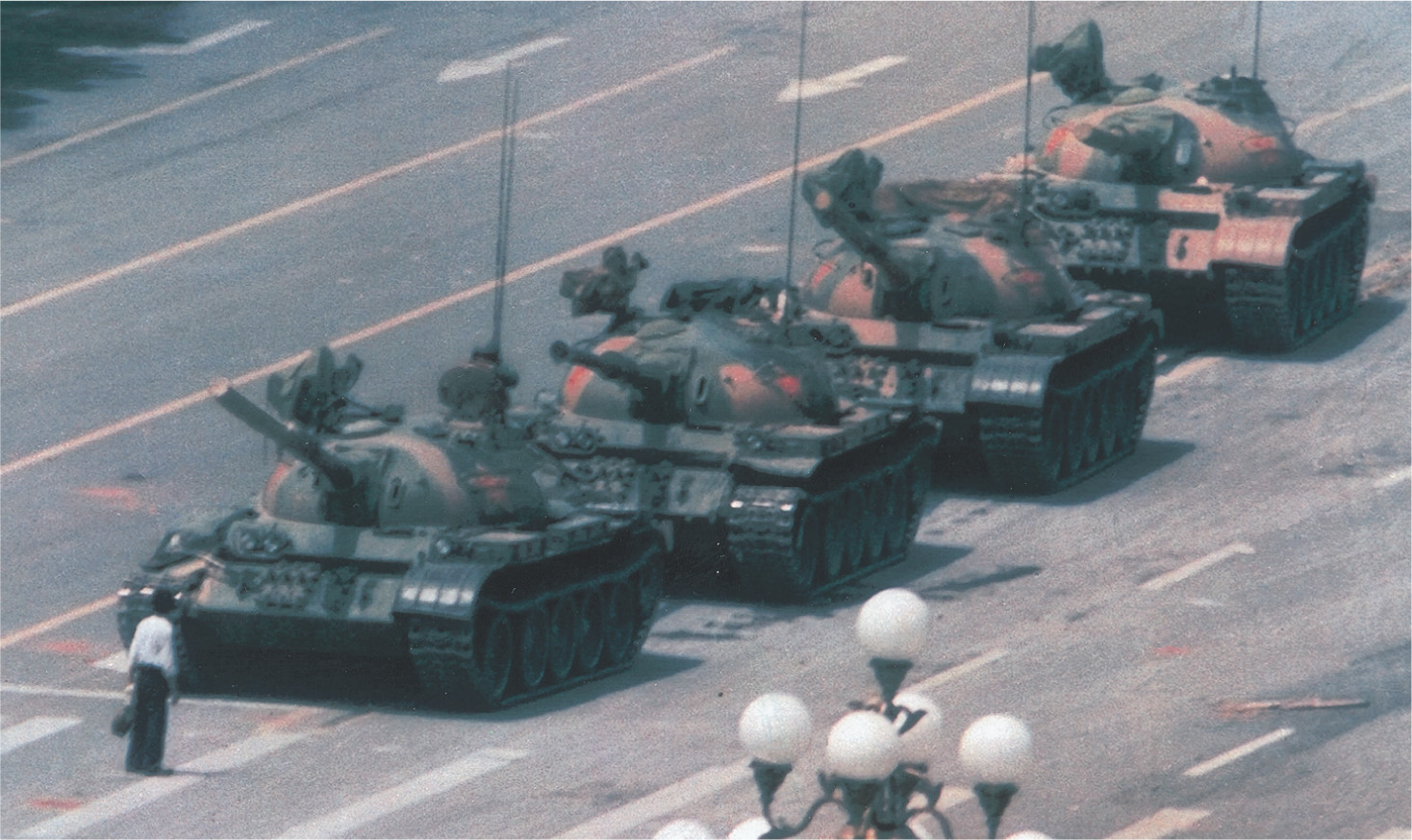 photo: a man stands alone in front of a line of tanks.