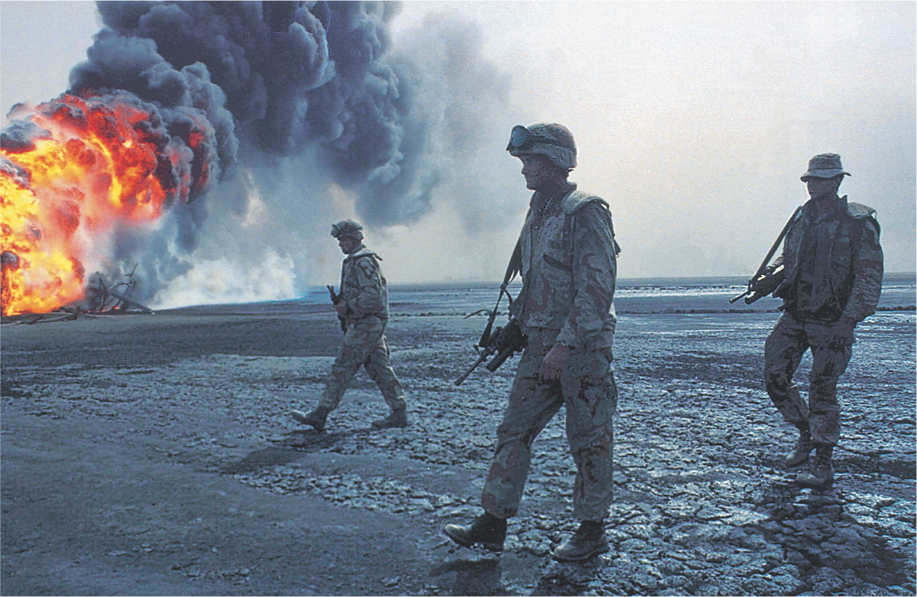 Soldiers walk near a blazing fire.
