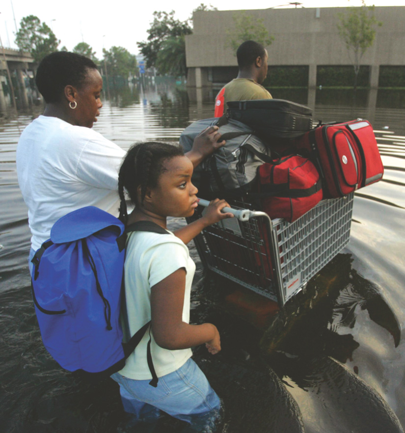 photo: a family pushes a shopping cart loaded with their possessions through waist-deep floodwater.