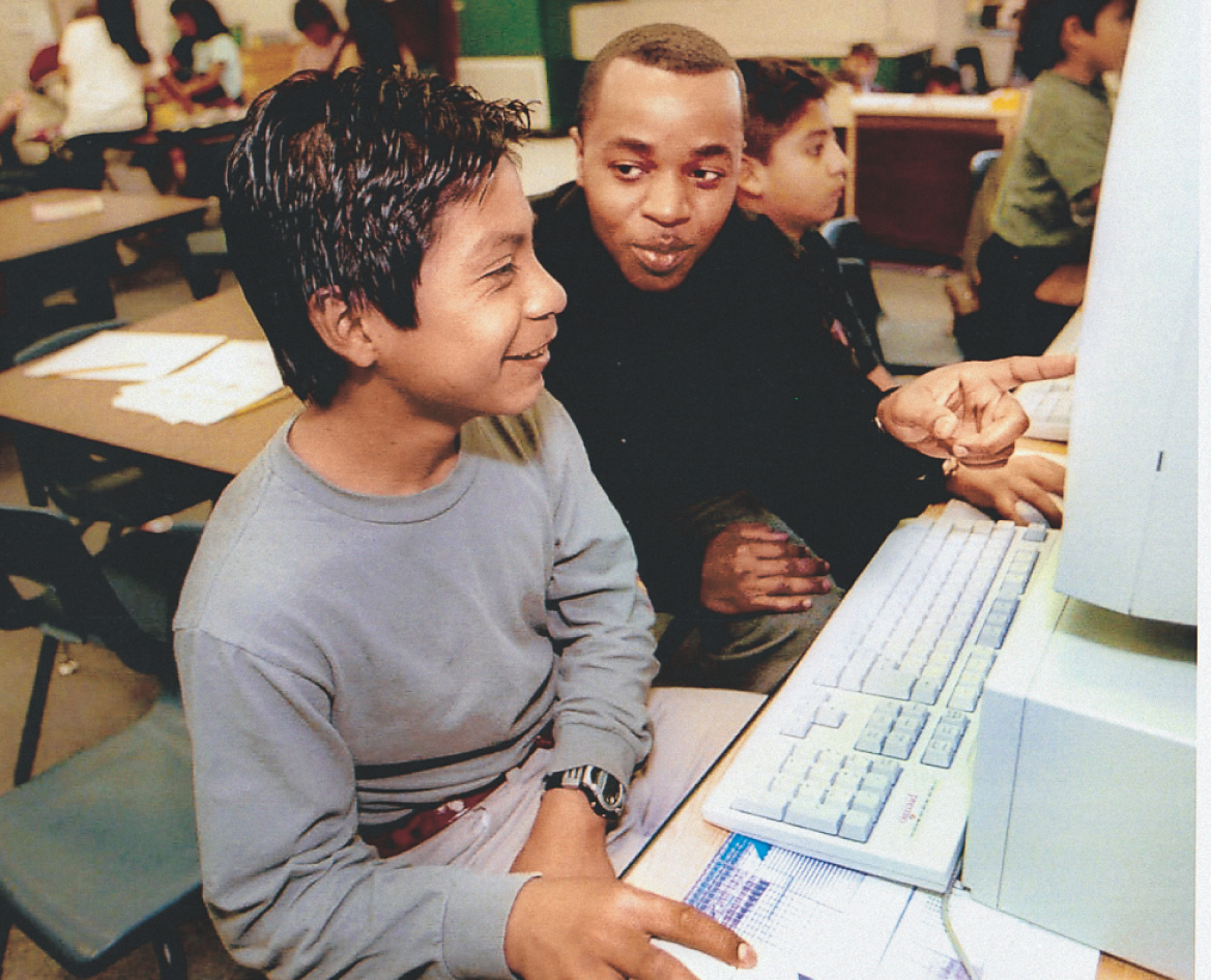 photo: a teacher helps a student use a computer.