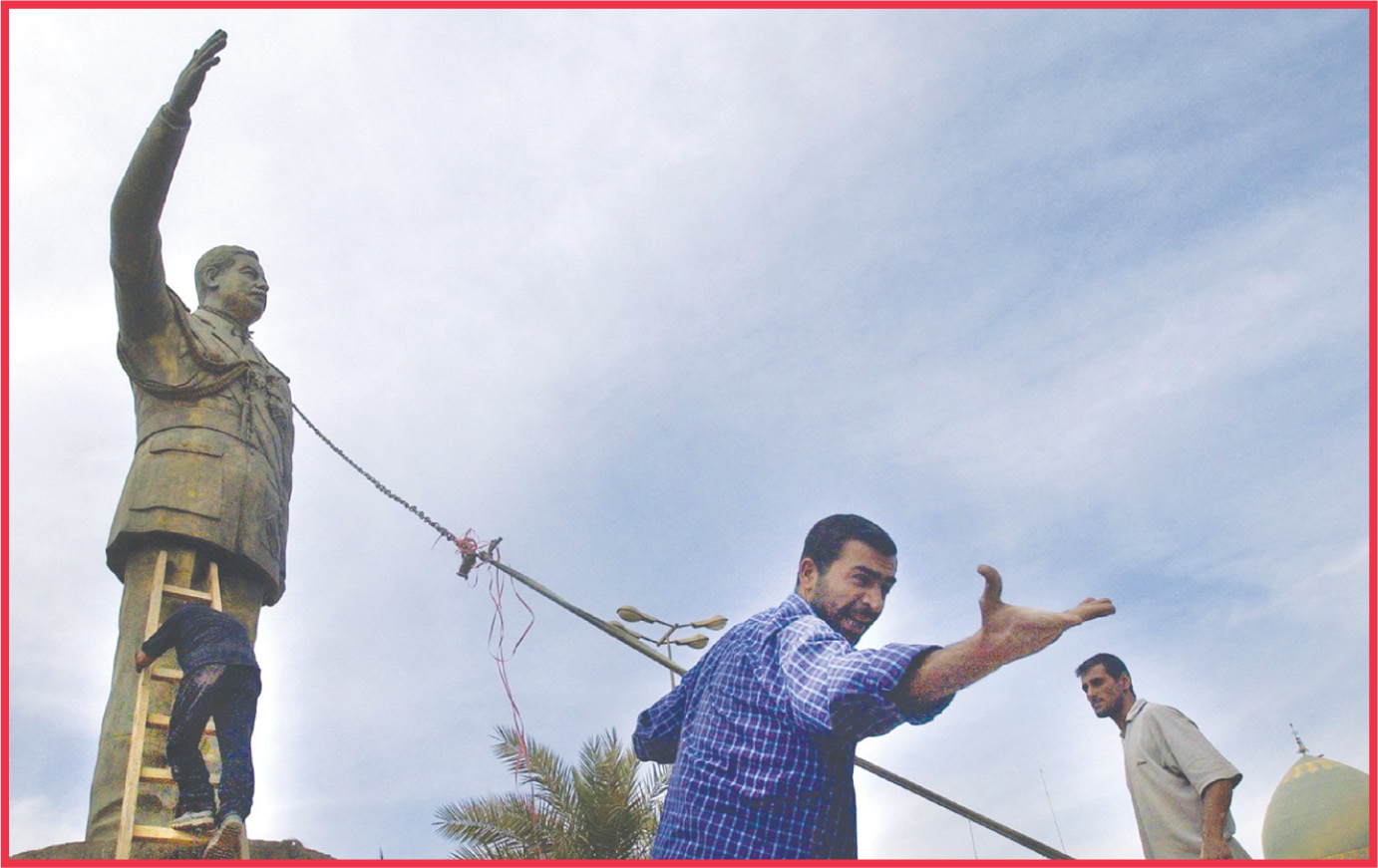photo: men attach a rope to a statue of Saddam Hussein.